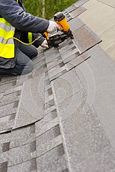 Workman using pneumatic nail gun install tile on roof of new house under construction