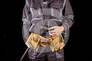 Workman in work clothes and tool belt. Production worker with a drill in his hand