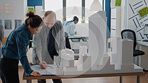 Workmates analyzing maquette and blueprints plan on table to work on architecture and building model.