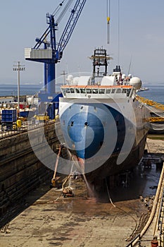 Workmen cleaning the hull of a merchant ship in the dry dock of a shipyard in Gibraltar. Cranes, heavy tools, ships