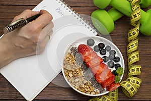 Workout and fitness dieting copy space diary. Dumbbell, vegetable smoothies and measuring tape on rustic wooden table