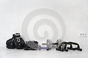 Workout at home concept. Dumbbells, push up bars, training sneakers, boxing gloves are on the room floor.