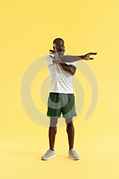 Workout. Man stretching arm, warming up on yellow background