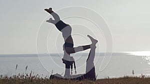 Workout at nature background, sporty couple practicing acro yoga on meadow on background of sea and sunset