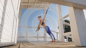 workout outdoors. suspension straps. workout with straps. Athletic young woman is doing all-body resistance exercises