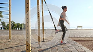 workout outdoors. suspension straps. workout with straps. Athletic young woman is doing all-body resistance exercises