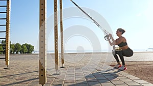 workout outdoors. suspension straps. workout with straps. Athletic young woman is doing all-body resistance exercises