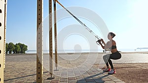 workout outdoors. suspension straps. workout with straps. Athletic young woman is doing all-body resistance exercises