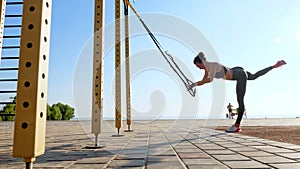 workout outdoors. suspension straps. workout with straps. Athletic young woman is doing all-body resistance exercises