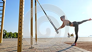 workout outdoors. suspension straps. workout with straps. Athletic young woman is doing all-body resistance exercises