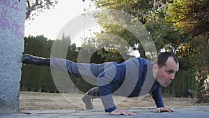 Workout with personal trainer outdoors. Male athlete in military style boots and trousers doing raised leg push-ups in a