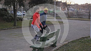 Workout with personal trainer outdoors. Young attractive woman in red bubble jacket and male fitness coach doing step