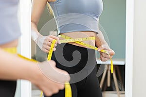 Workout, Slim asian young woman standing hand in measuring tape around waist her in fit sportswear, looking reflect in mirror at