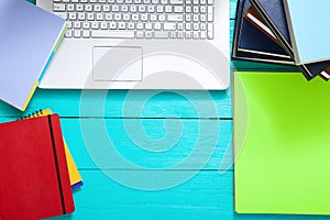 Workplace with books, keyboard, notebooks and other accessories on blue wooden background. Top view and copy space