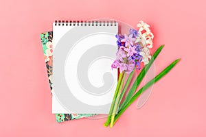 Workplace with bouquet of hyacinths flowers, white notepad on pink background Flat lay Top view copy space Mock up Sesonal,