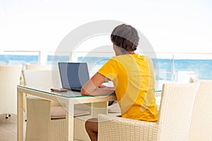 Workplace in a cafe with a sea view. Man working on a laptop in a cafe. Copy space. Mock up