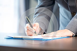 Workplace closeup person professional businesswoman sitting at desk hold pen signing or signature contract paper. Employee woman