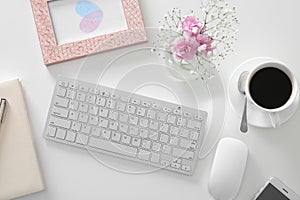 Workplace with computer keyboard and bouquet of beautiful pink flowers on white table, top view