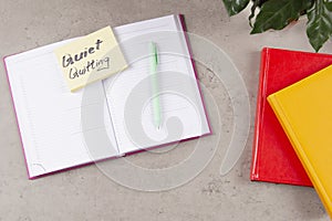 Workplace desk with paper business notebook planner with sticky note and text Quiet Quitting on it. Work-to-rule, in
