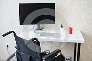 Workplace for a disabled person. Wheelchair at the table with a computer.