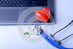 Workplace of doctor with laptop, stethoscope, red heart and assorted pils on white table. top view.