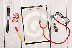 Workplace of doctor. Red stethoscope, clipboard, glasses, watch and pills on white wooden table