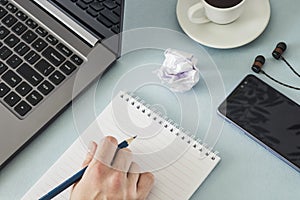 Workplace. Female hand with a notebook and pencil laptop smartphone headphones cup of coffee.