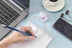 Workplace. Female hands with a notebook and pencil laptop smartphone headphones cup of coffee.