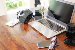 Workplace of a female photographer with laptop, camera and lenses on a wooden table near the window,  copy space