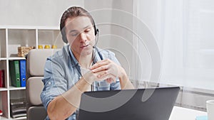 Workplace of freelancer. Employee works at home office using computer and headset. Young man is having a conference call