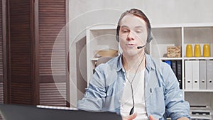 Workplace of freelancer. Employee works at home office using computer and headset. Young man is having a conference call