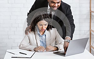 Workplace harassment. Boss touching his young attractive female assistant while she working on laptop at office