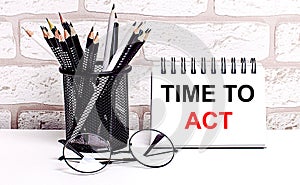 A workplace in the house with glasses, pencils in a stand and a notebook with text TIME TO ACT on a brick wall background. Home