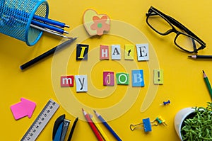 Workplace with I Hate My Job sign of carved letters and office supplies on yellow background