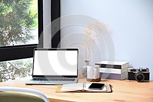 Workplace with laptop computer, books and camera on wooden table.