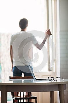 Workplace with laptop and glasses and man silhouette near window