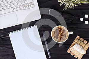 Workplace mockup with a cup of cappuccino coffee on a wooden dark table with a laptop and notepad