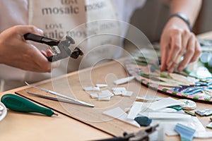 Workplace of the mosaic master: women`s hands holding tool for mosaic details in the process of making a mosaic