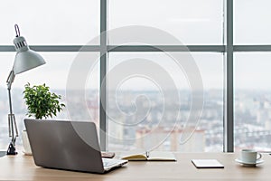 Workplace with notebook laptop Comfortable work table in office windows and city view.