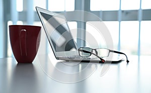 Workplace with notebook laptop, reading glasses and red coffee mug table