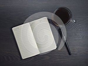 Workplace with notebook, pen and glass coffee mug on wooden background