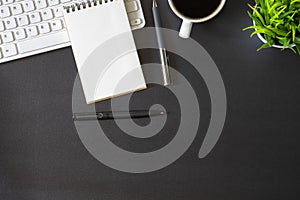 Workplace office with dark black desk. Top view from above of keyboard with notepad and coffee cup. Space for modern creative work