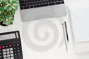 Workplace in office - desk with laptop, calculator, stack of papers, notebook, a pen and a green plant.