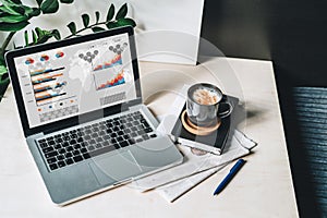 Workplace without people, close-up of laptop with graphs, charts, diagrams on screen on white table, desk.