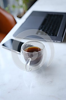 workplace with phone laptop and transparent cup of coffee in home office on white marble desk with brown leathern chair