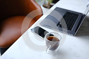 workplace with phone laptop and transparent cup of coffee in home office on white marble desk with brown leathern chair