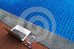 Workplace at the resort. Laptop and smartphone glasses near blue swimming pool. Modern Gadgets.