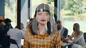 Workplace safety during pandemic. Portrait of young smiling Caucasian business woman in plastic face shield slow motion.