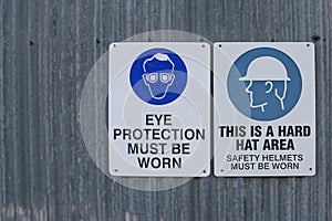 Workplace safety signs directing that eye protection and hard hat safety helments must be worn in the area