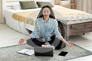 Workplace stress management. Calm young woman meditating with closed eyes in front of laptop pc at home, full length